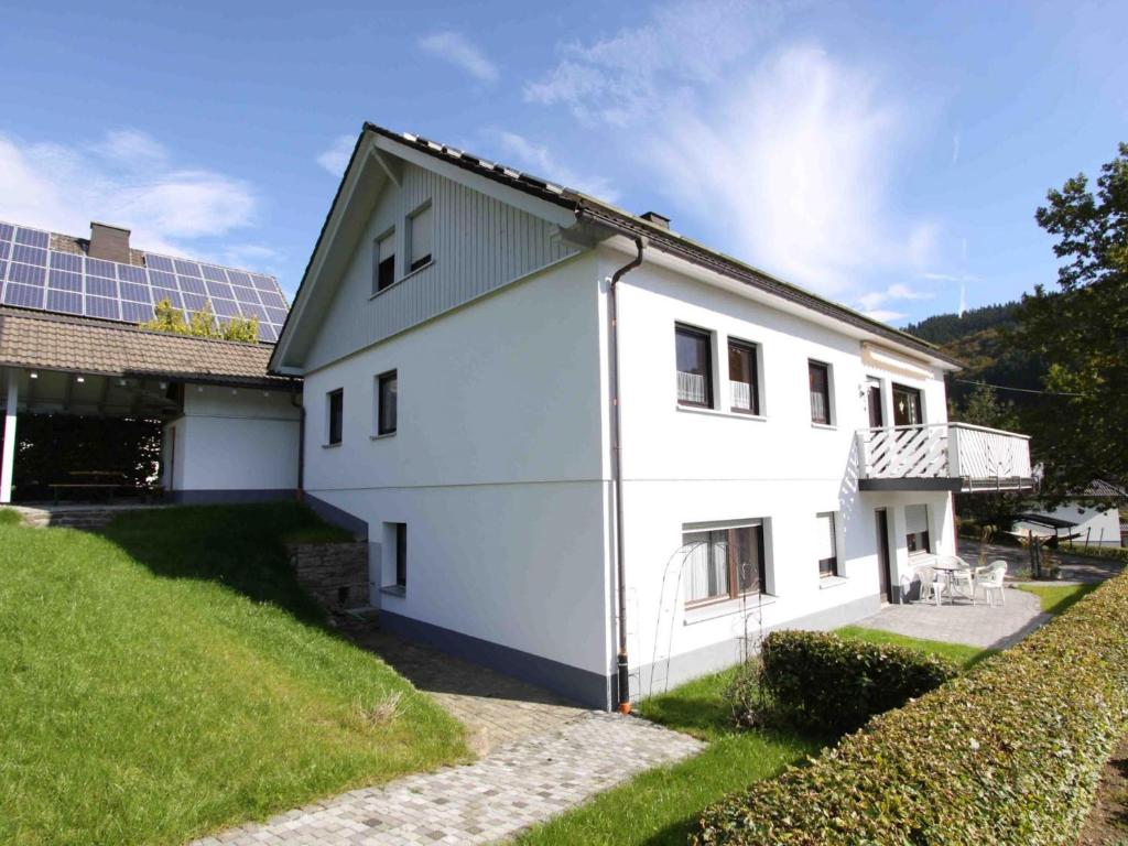 a white house with a green yard and a building at Haus Wanderglück in Schmallenberg