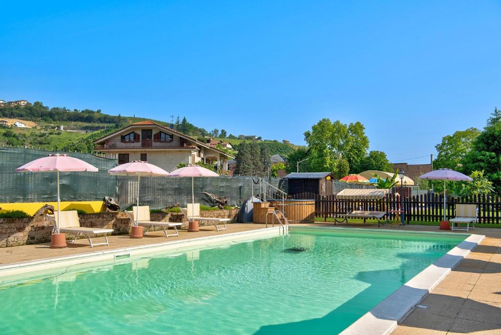a swimming pool with umbrellas and chairs and a house at Clematis in Cisterna dʼAsti