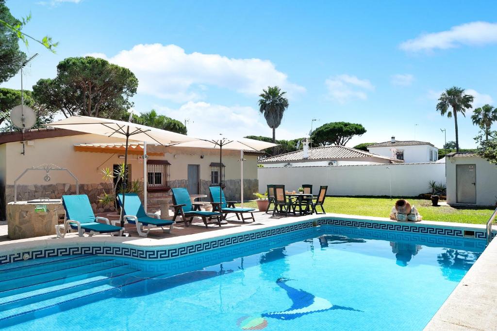 a swimming pool with blue chairs and a house at Chalet Los Paul in Chiclana de la Frontera
