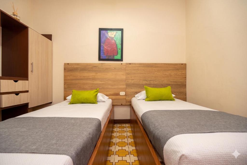 two beds in a small room with green pillows at Hotel Skal Inn in Barranquilla