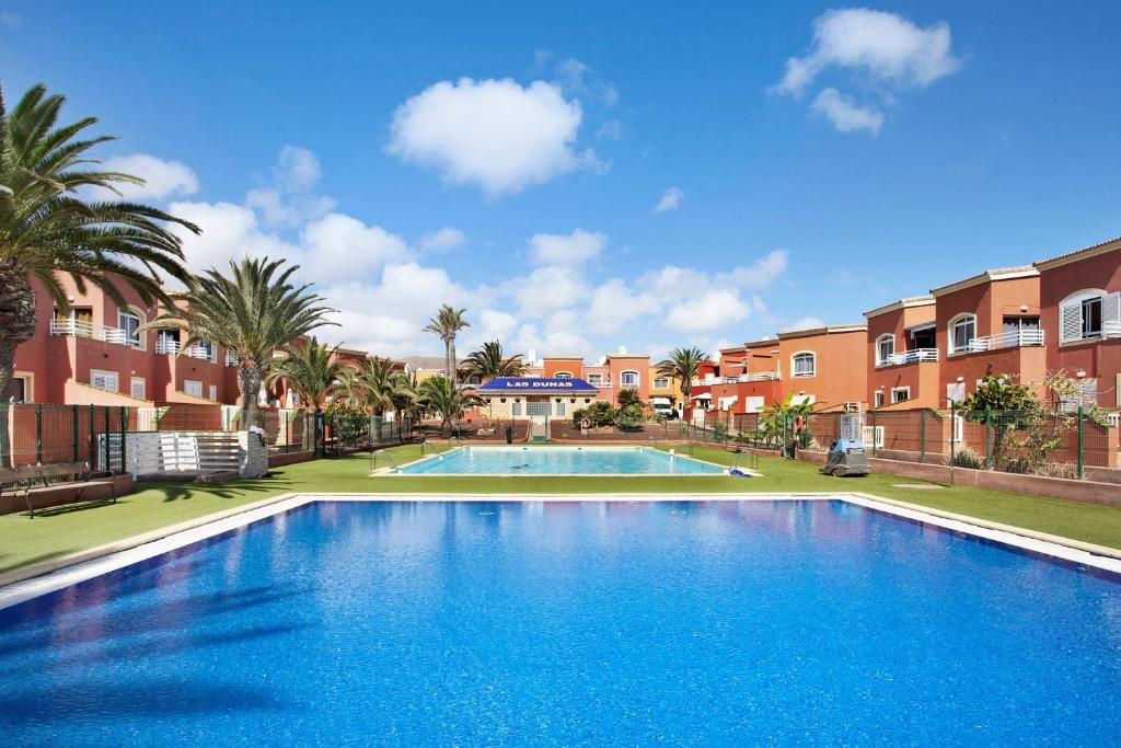 a large swimming pool with palm trees and buildings at Little Dunes in Corralejo