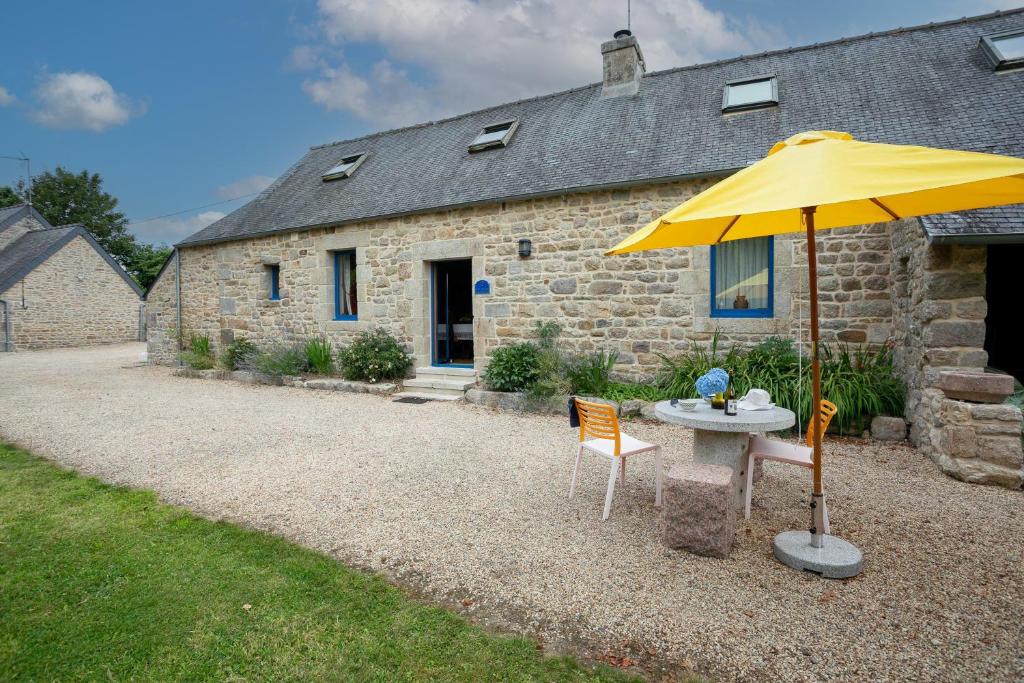 a table with a yellow umbrella in front of a stone house at Gîte Ty Coz in Lanvellec