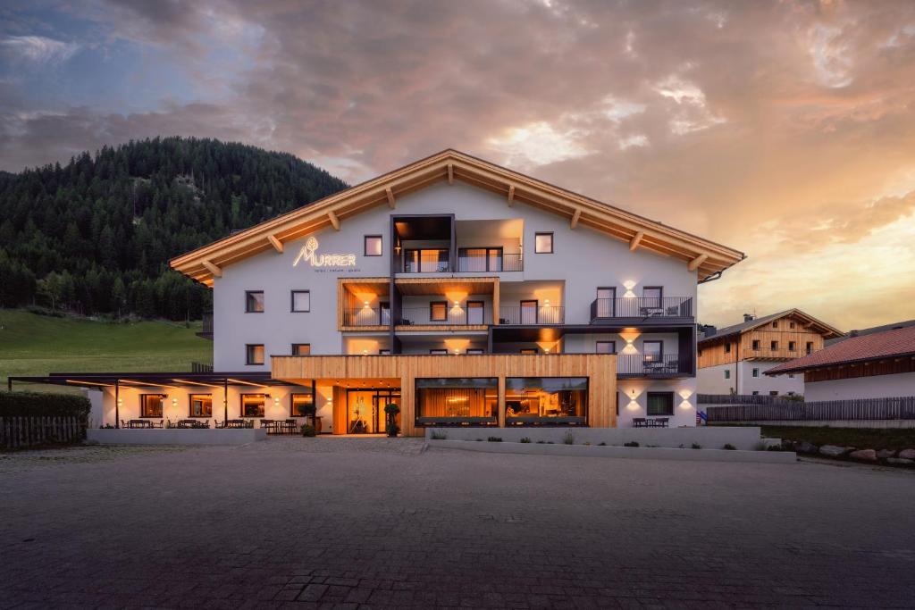 Ein großes weißes Gebäude vor dem Hintergrund eines Sonnenuntergangs in der Unterkunft Hotel Murrer relaxe.nature.gusto in Sarntal