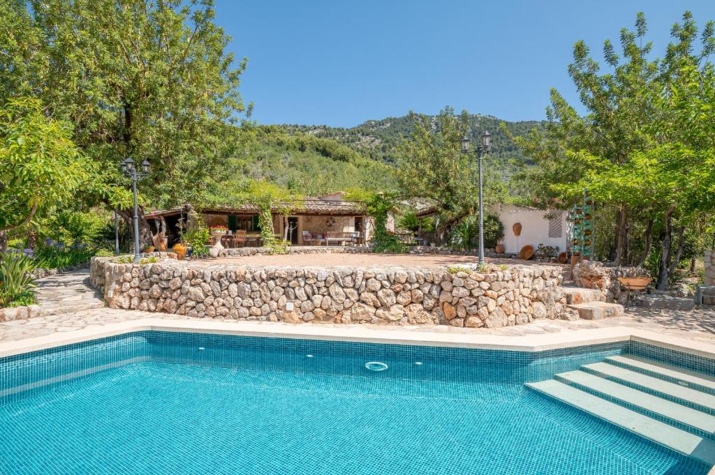 a swimming pool in front of a house with a stone wall at S Olivar Major in Fornalutx