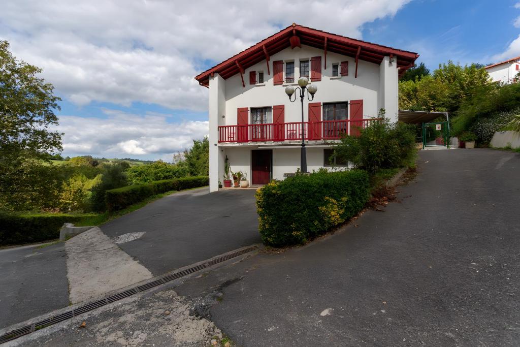 a white house with a red balcony and a driveway at Maison Xara-heguia in Hasparren