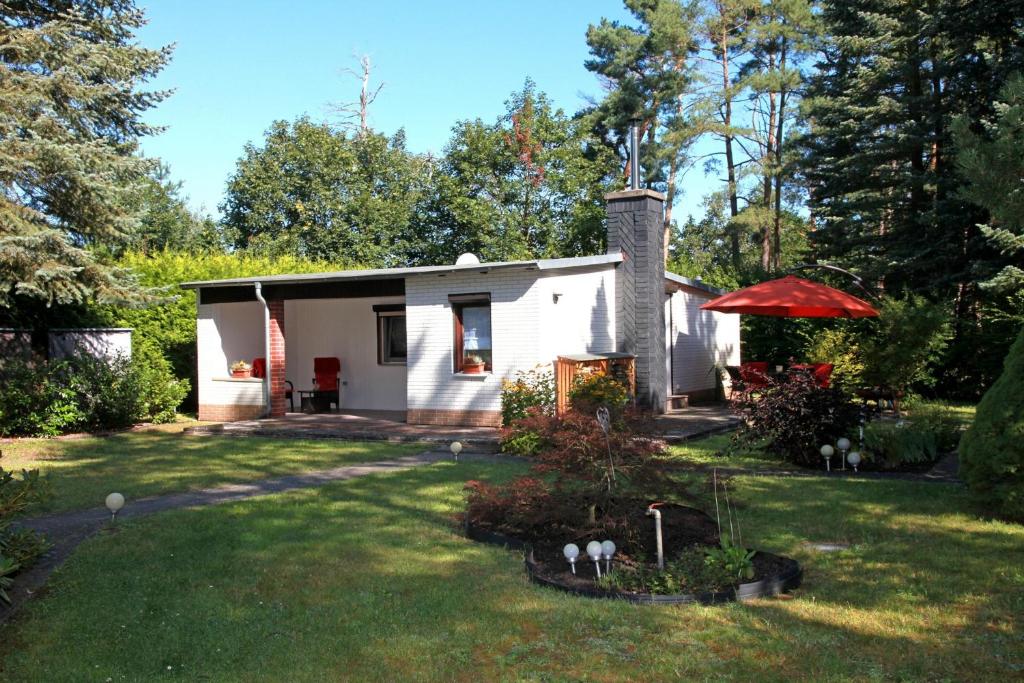 a small white cottage with a red umbrella in a yard at Haus Waldidyll am Briesensee in Neu Zauche