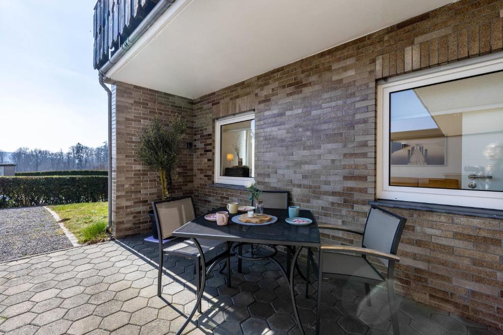 a patio with a table and chairs and a brick wall at Ferienwohnung Frank in Melschede