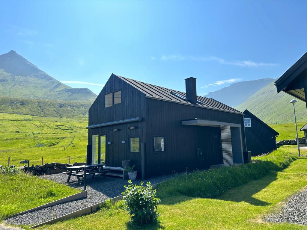 a black house in a field with mountains in the background at Luxury Cottage with Stunning Views - Okkara summarhús við Gjógv in Við Gjógv