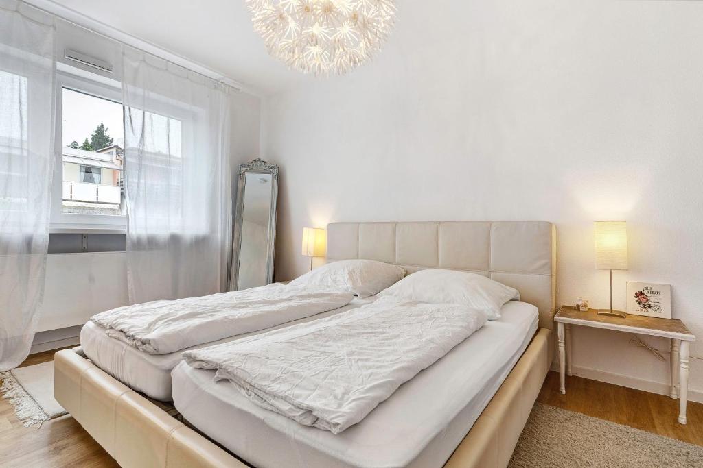a white bedroom with a large bed and a chandelier at Haus 15 in Offenburg
