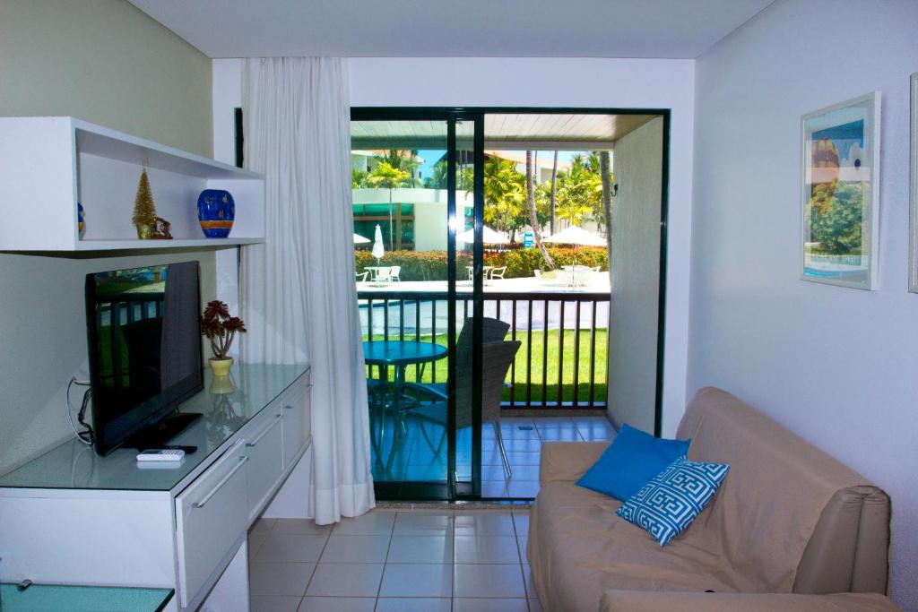 ein Wohnzimmer mit einem Sofa, einem TV und einem Balkon in der Unterkunft FLAT MARULHOS SUÍTES E RESORT in Porto De Galinhas