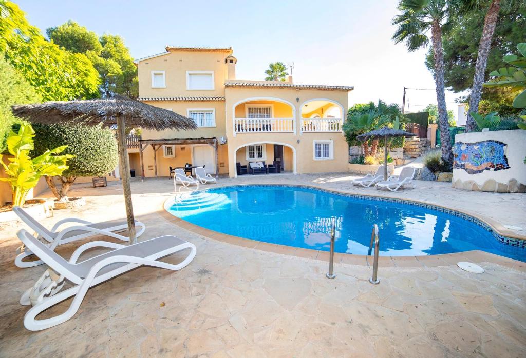 a house with a swimming pool with chairs and an umbrella at Verano in Calpe