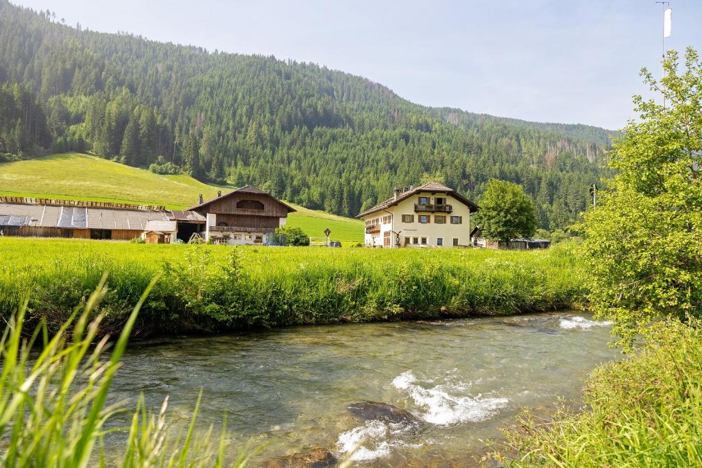 a river in a field with houses and a mountain at Untersinnerhof Gsies in Valle Di Casies