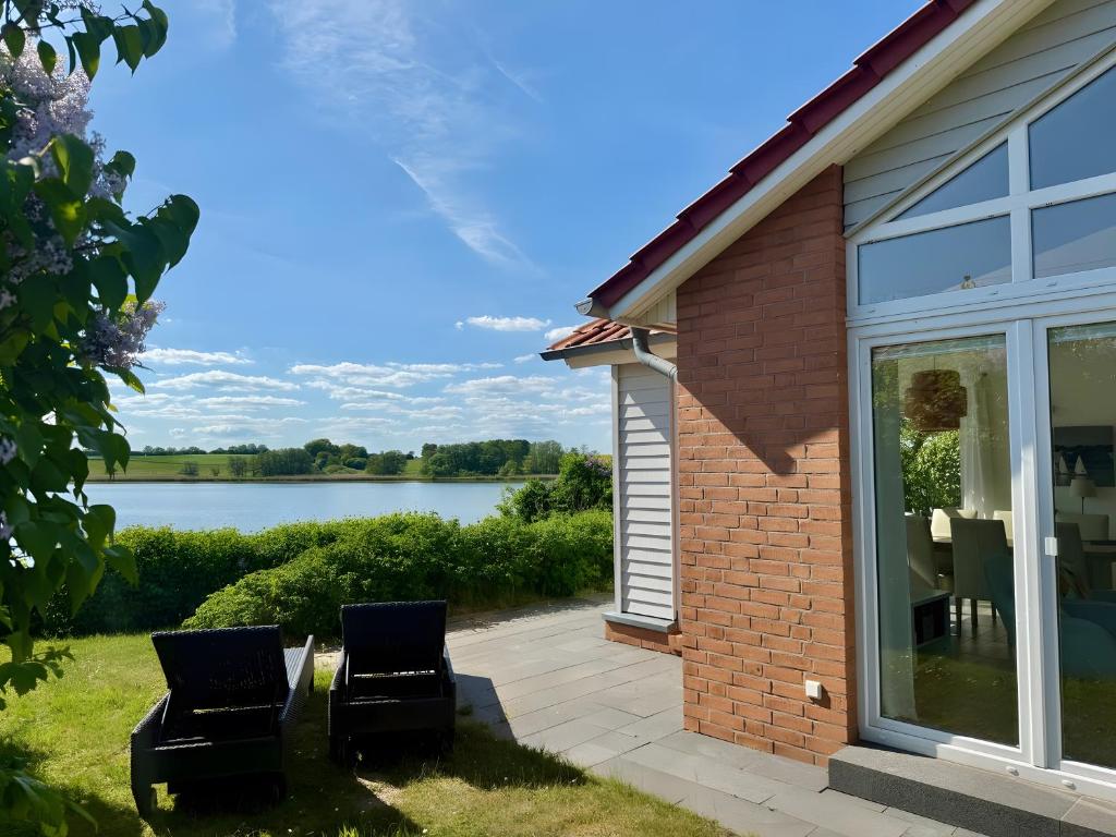 a house with two chairs on a patio next to a lake at Brombeeruferhaus in Kosel