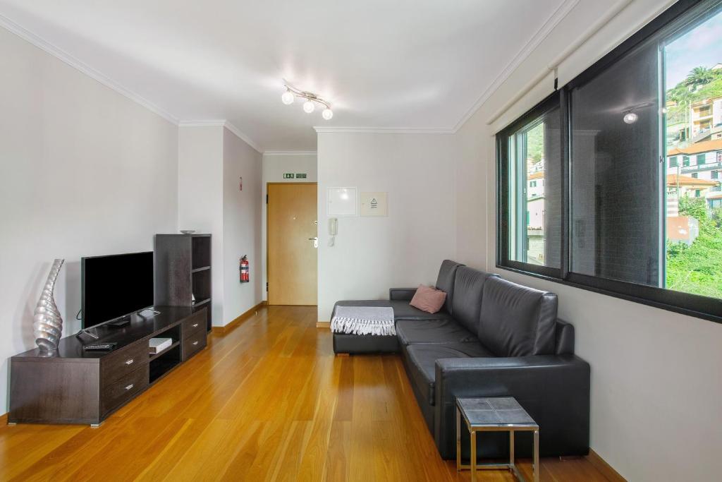 a living room with a black couch and a tv at Apartamento Eden in Machico