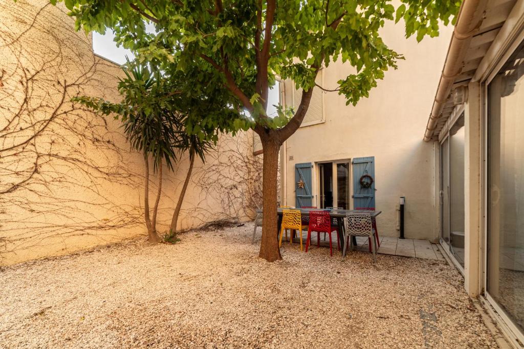 a table and chairs under a tree next to a building at Maison type Canetoise prox plage in Canet-en-Roussillon