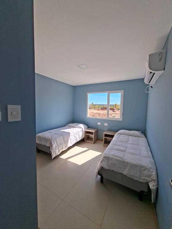 two beds in a room with blue walls and a window at El Portal Los Álamos in Rincon de los Sauces