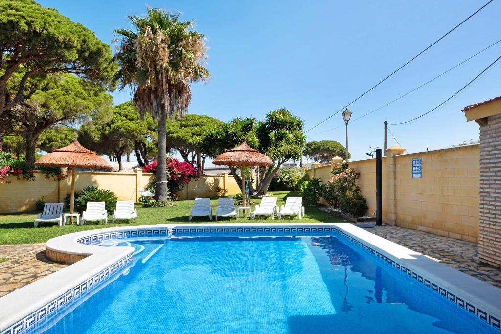 a swimming pool in a yard with chairs and umbrellas at Magnolia A - Solo Familias in Conil de la Frontera