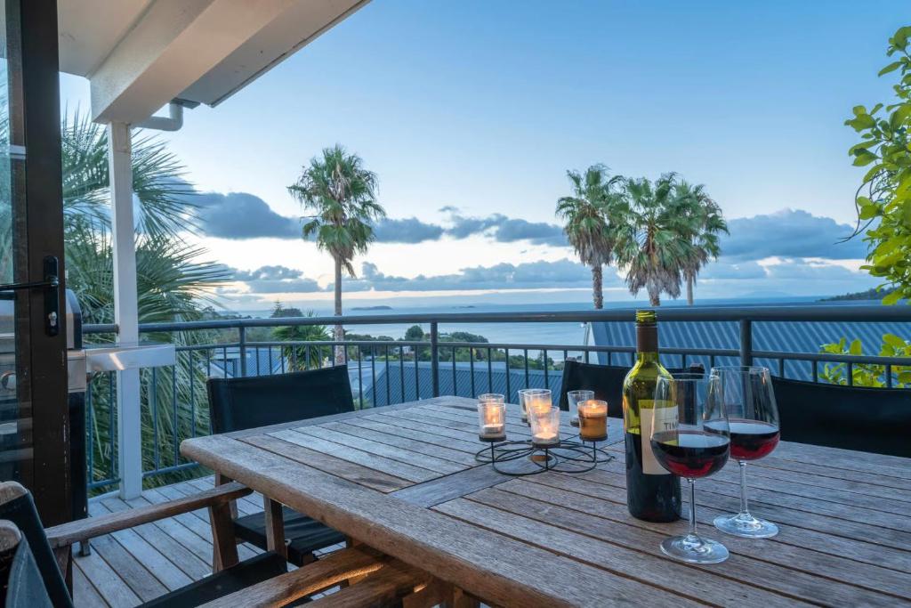 a wooden table with two glasses of wine on a balcony at Premium Seaview Villa in Waiheke Island