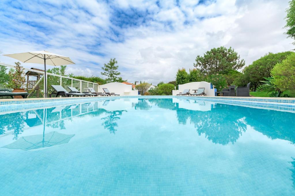 a large swimming pool with an umbrella and chairs at Canto do Sol - Selão da Eira in Pedreneiras