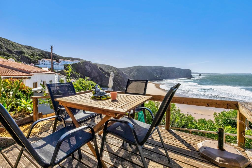 a wooden table and chairs on a deck with the ocean at Abrigo do Pescador in Aljezur