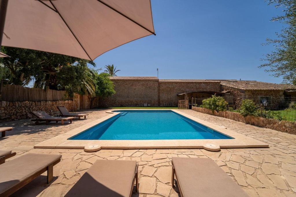 a swimming pool with an umbrella and some benches at Cugulutx in Llucmajor