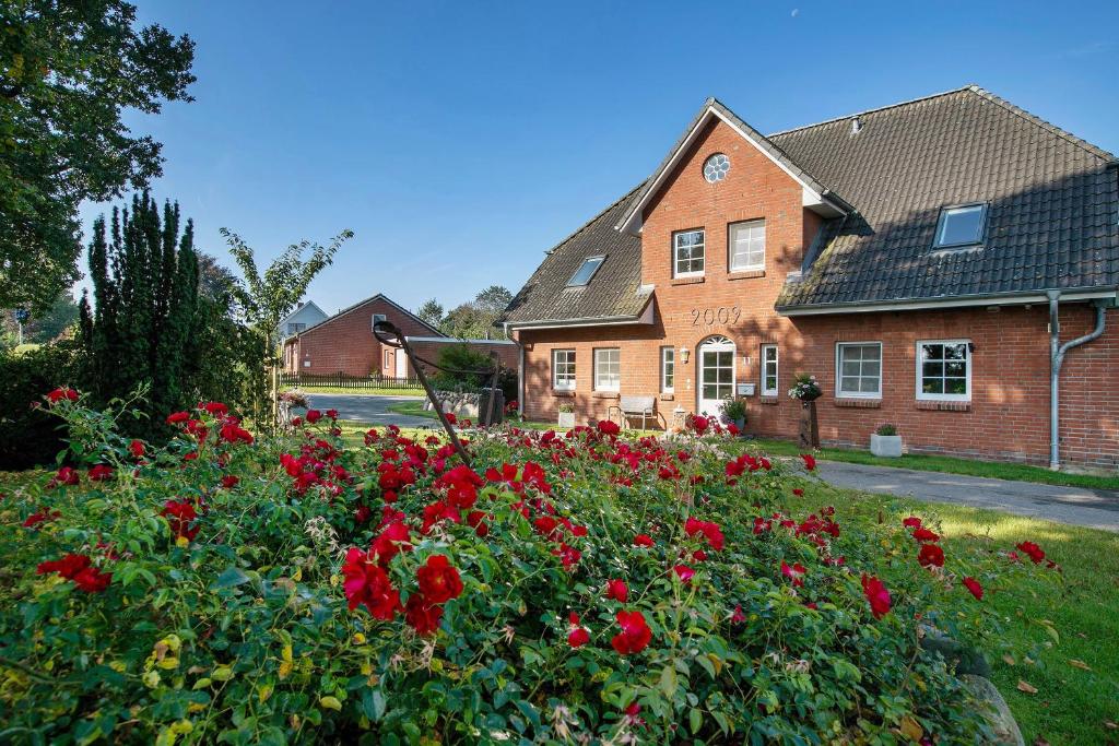 a house with a garden of red flowers in front of it at Ferienwohnung Andresen Högel in Högel