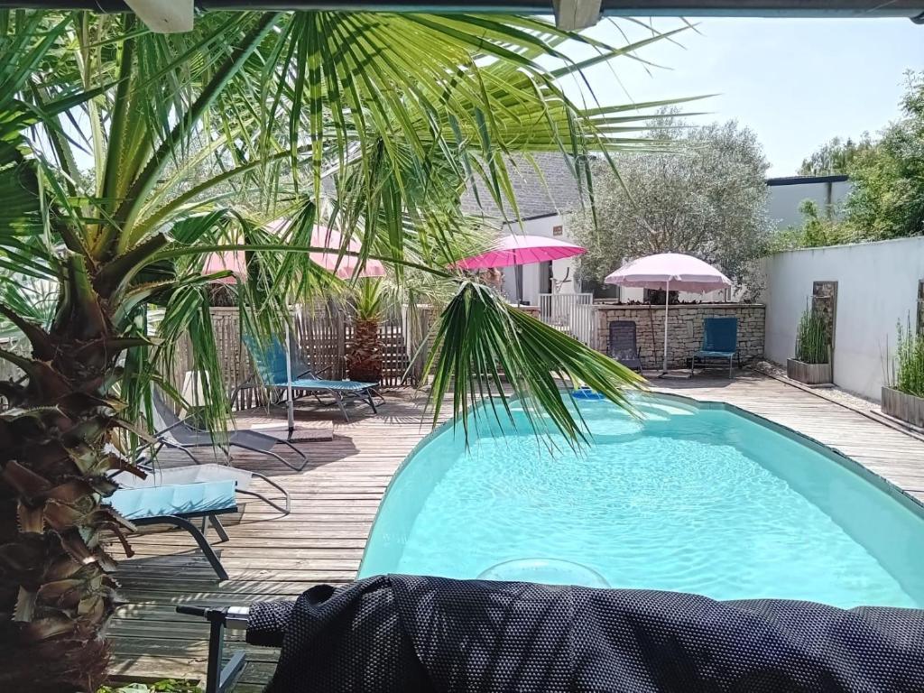 a pool with a palm tree and chairs and umbrellas at Villa la forge expérience bien-être in Nuaillé-dʼAunis