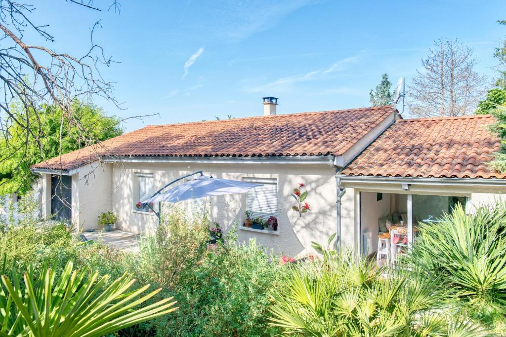 a white house with an umbrella in the garden at Gite L'oiseau Du Paradis in Ribérac