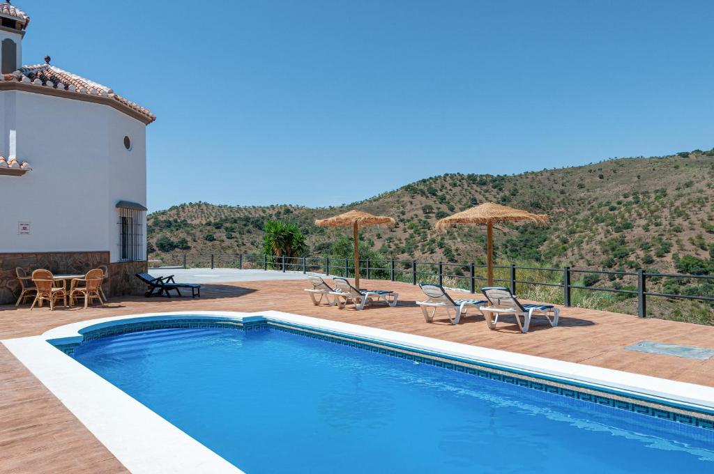 a swimming pool with chairs and umbrellas on a patio at Sunset El Tejar in Almogía