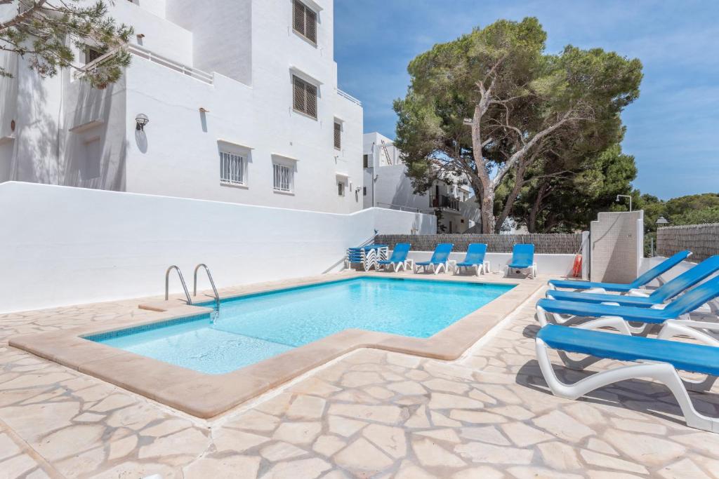 a swimming pool with blue lounge chairs and a building at Apartamentos Karin 2ºe in Cala d´Or