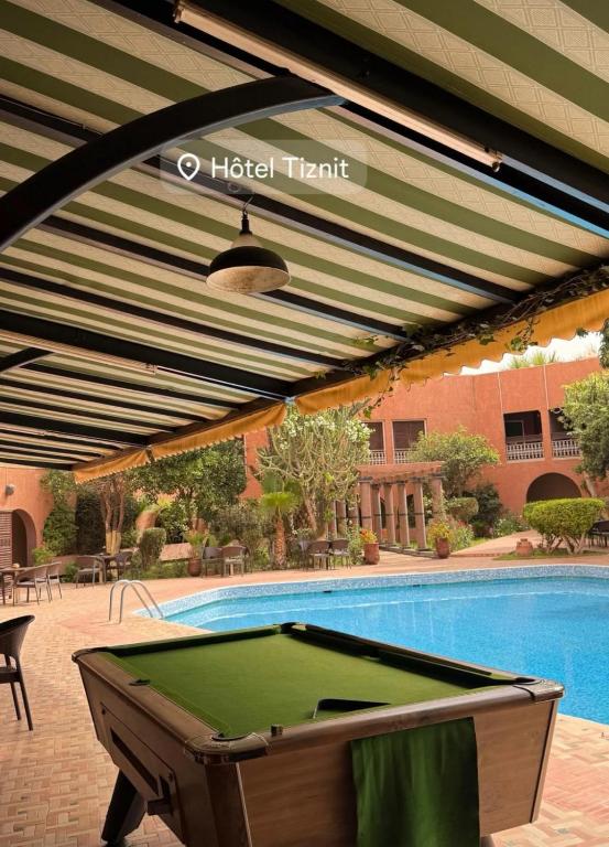 a pool table under awning next to a swimming pool at Hotel Tiznit in Tiznit