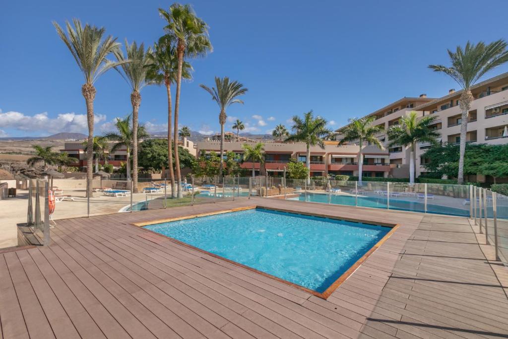 a swimming pool with palm trees and a building at Bugalú Playa Paraíso in Adeje