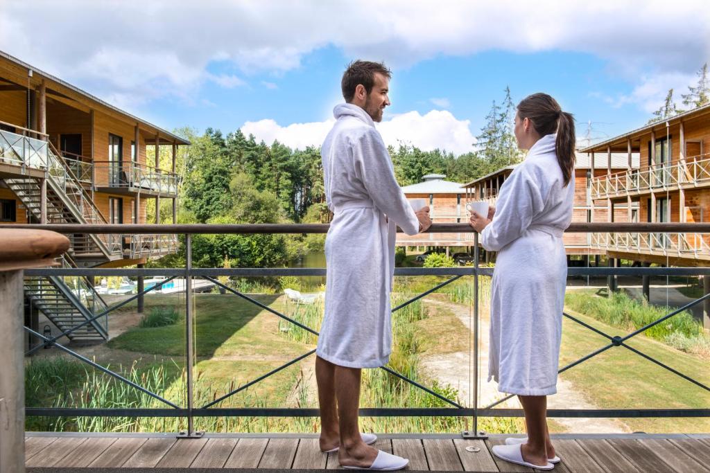 un uomo e una donna in vestaglia bianca su un balcone di Domaine de Cicé-Blossac, Resort Spa & Golf a Bruz