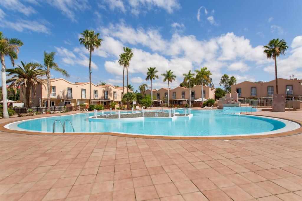 a swimming pool with palm trees and houses at Maspalomas Green Oasis in San Bartolomé
