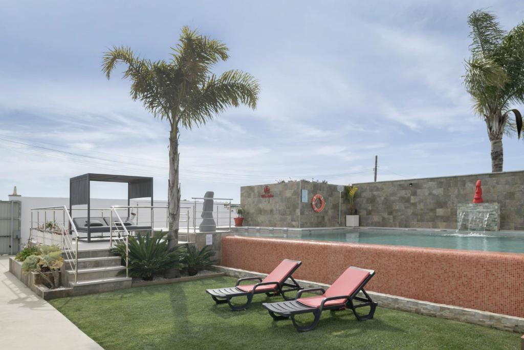 a swimming pool with two pink chairs and palm trees at Villa Adán con Piscina Majestuosa in Cádiz