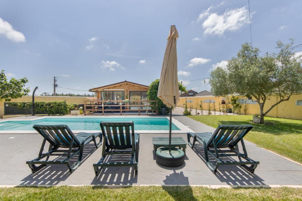 a pool with three chairs and an umbrella at Casinha Saragoça e Vergueiro in Ponte de Vagos