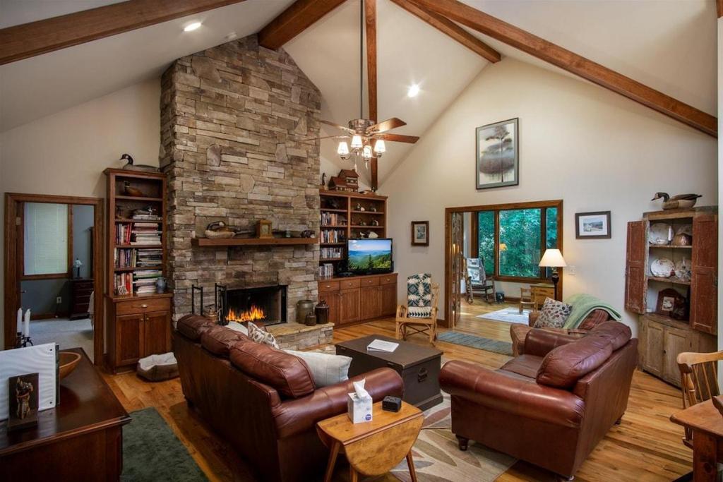 a living room with a stone fireplace and leather furniture at Pine Hill · Pine Hill in Sherwood Forest in Rosman