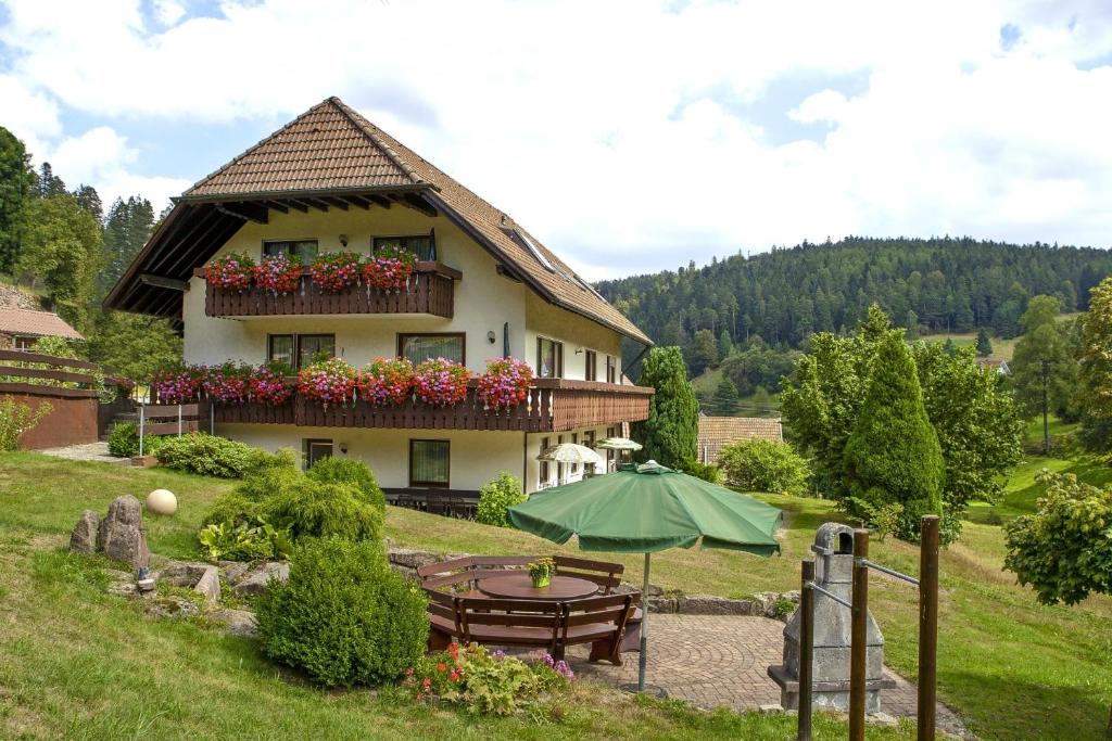 a house with a table and an umbrella in front of it at Haus Am Kaltenbach in Enzklösterle