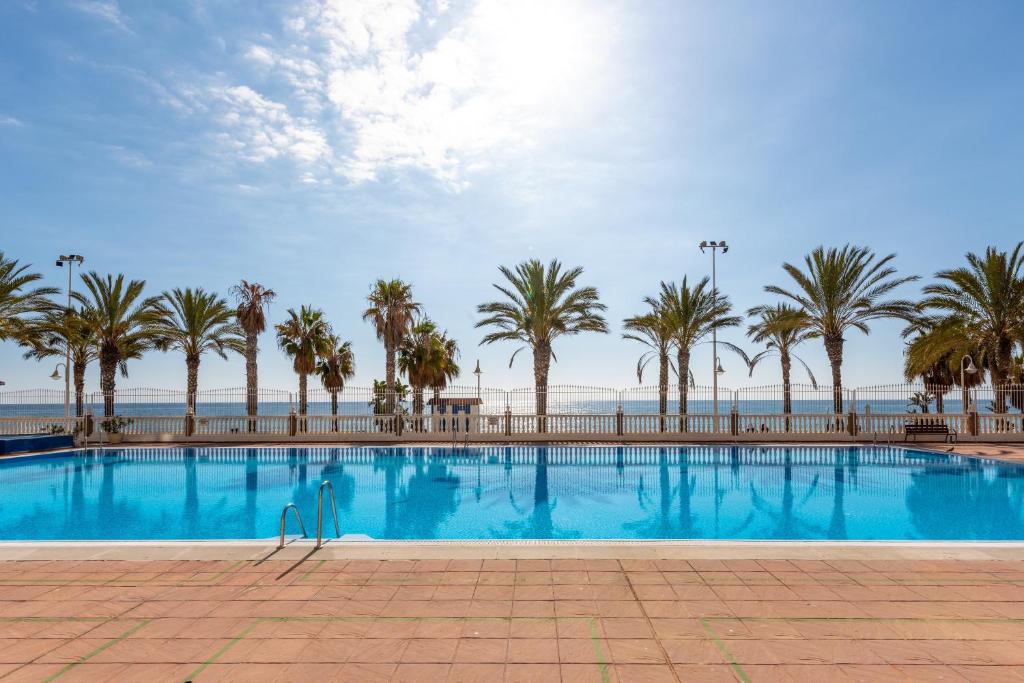 a swimming pool with palm trees and the ocean at 50 mts beach with sea views pool in Algarrobo-Costa