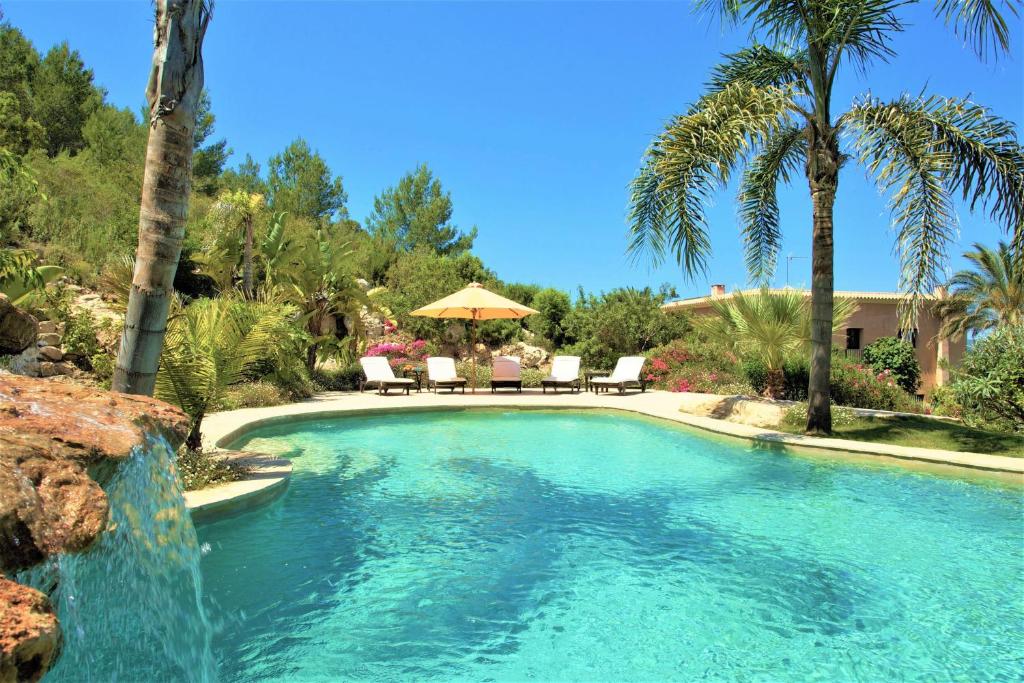 a swimming pool with a waterfall and palm trees at Sa Muntanya panorama in Santa Eularia des Riu