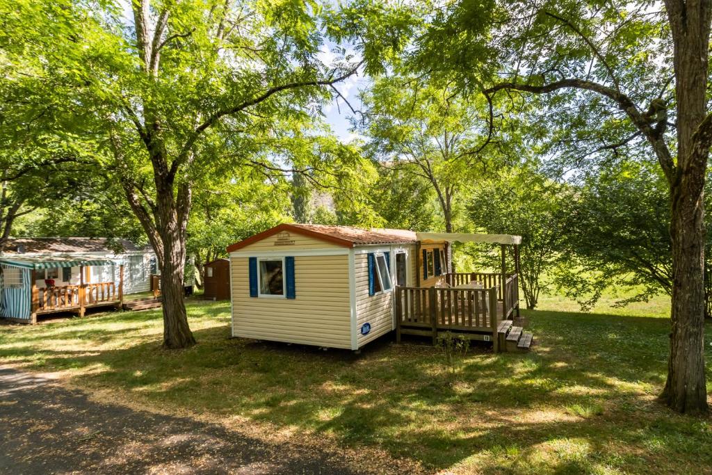 a small white cabin in a park with trees at Mobilhome La Clairière in Saint-Pompont