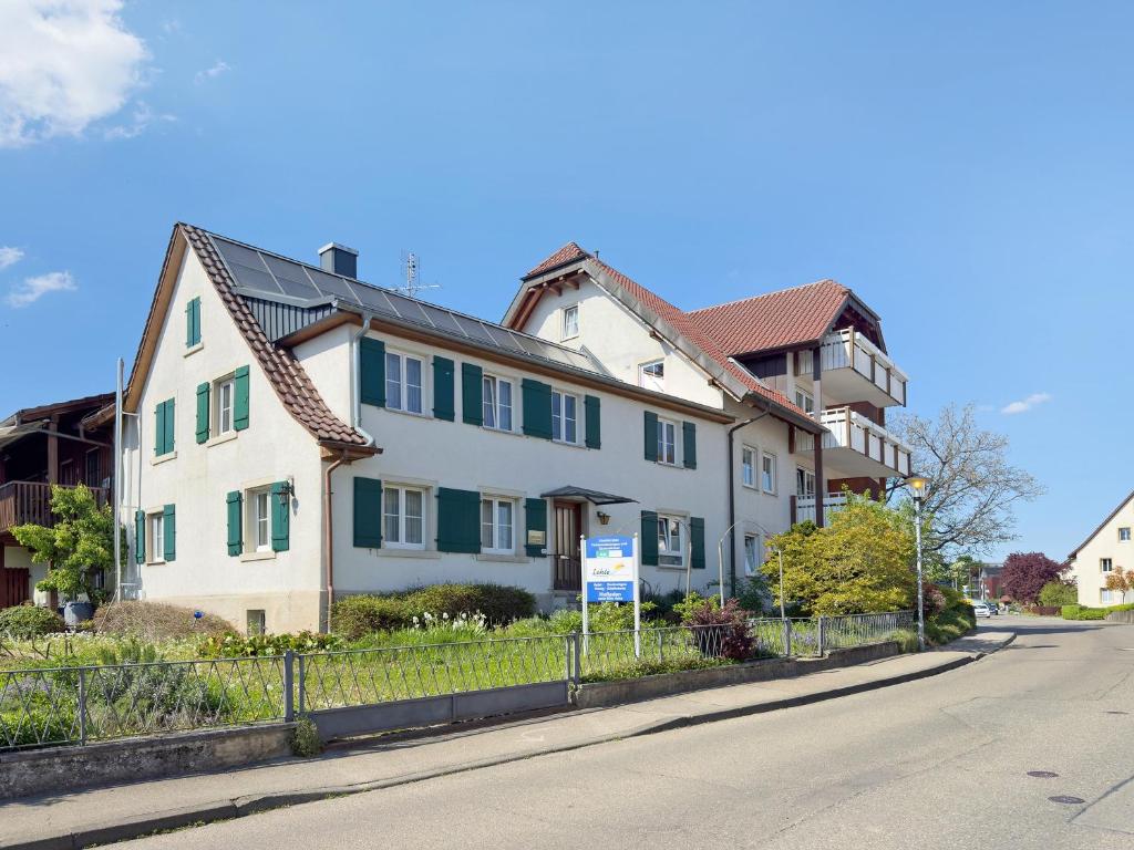 a white house with green shutters on a street at Obst- und Ferienhof Lehle in Immenstaad am Bodensee