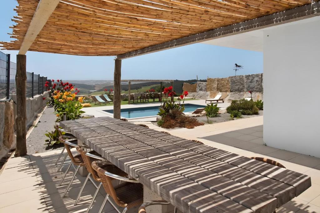 a wooden table and chairs on a patio with a pool at Peace House Lourinhã - Villa 8 in Lourinhã