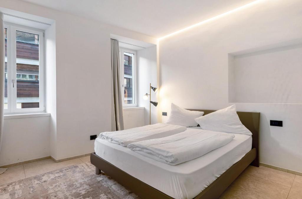 a white bedroom with a bed and two windows at App 103 Palazzo Cavour in Bolzano