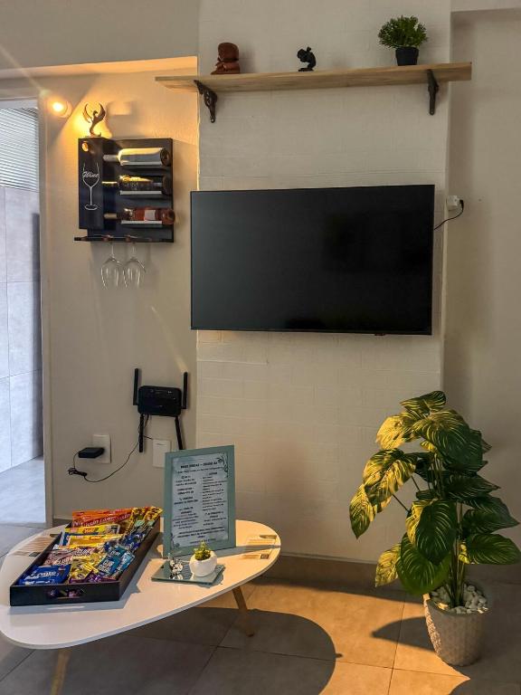 a living room with a table and a tv on a wall at Studio 43 - Central Coração de Franca in Franca