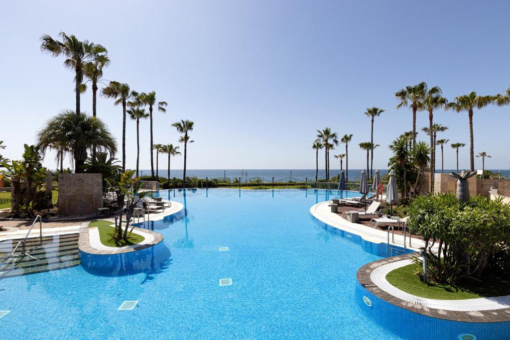 a large swimming pool with palm trees and the ocean at Exclusive frontline beach penthouse in Estepona