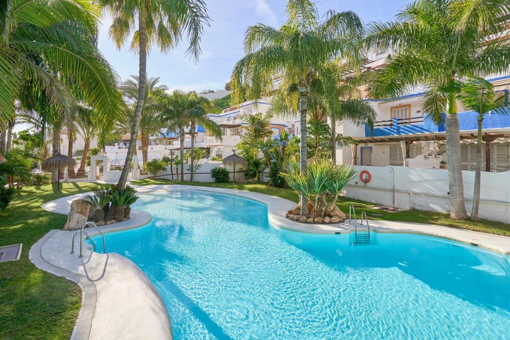 a swimming pool with palm trees in front of a building at La Casita Azul in Almuñécar