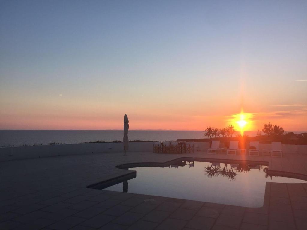 a sunset over the ocean with a statue and a pool at Villa Es Gallinots in Mahón