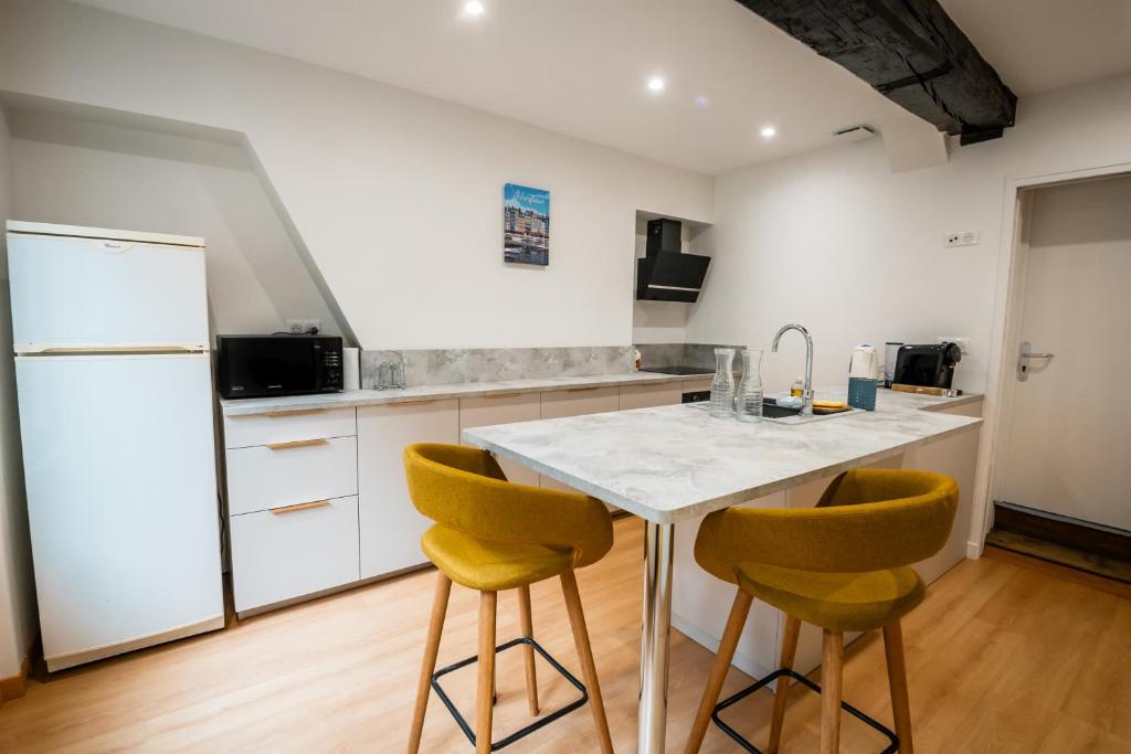 a kitchen with a white counter and yellow chairs at Murmures de la Risle in Pont-Audemer