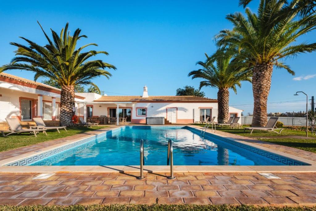 a swimming pool with palm trees in front of a house at Villa Las Rosas in Albufeira